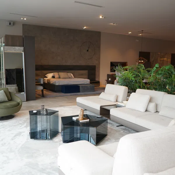 Modern living room and bedroom area featuring neutral sofas, green chair, glass tables, and indoor plants in open space.