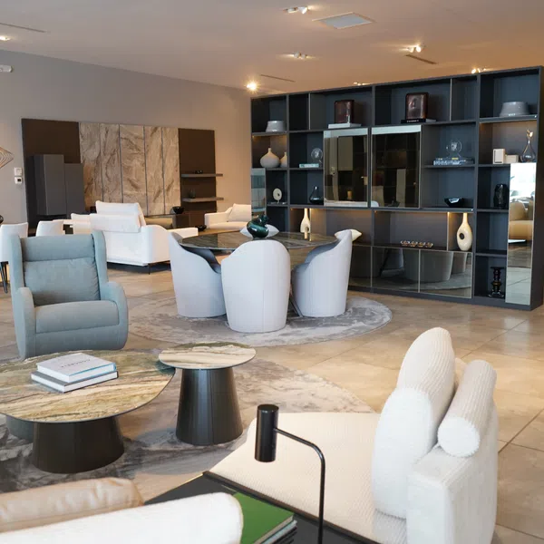 Modern living room with white and gray furniture, round tables, large bookshelf, and decorative vases in spacious interior.