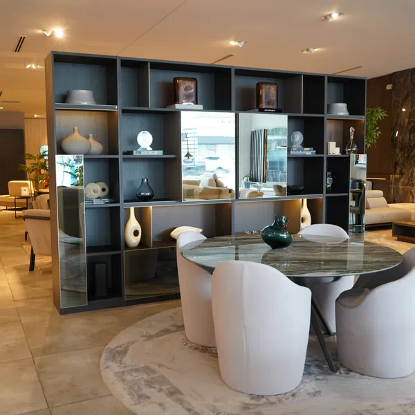 Modern living room with marble dining table, white chairs, open shelving, and neutral sofas in warm lighting