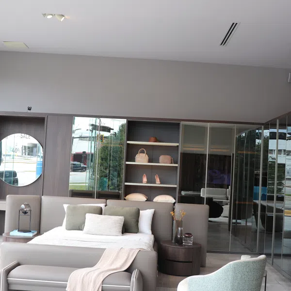 Modern bedroom interior with a large bed, soft pillows, a bench, and mirrored wardrobe doors in neutral tones.