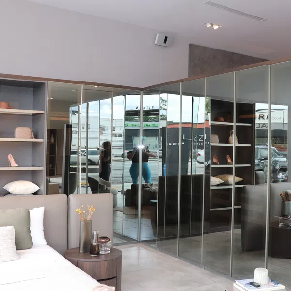 Modern bedroom with mirrored closet doors, shelves with shoes and pillows, and a bed with cushions.