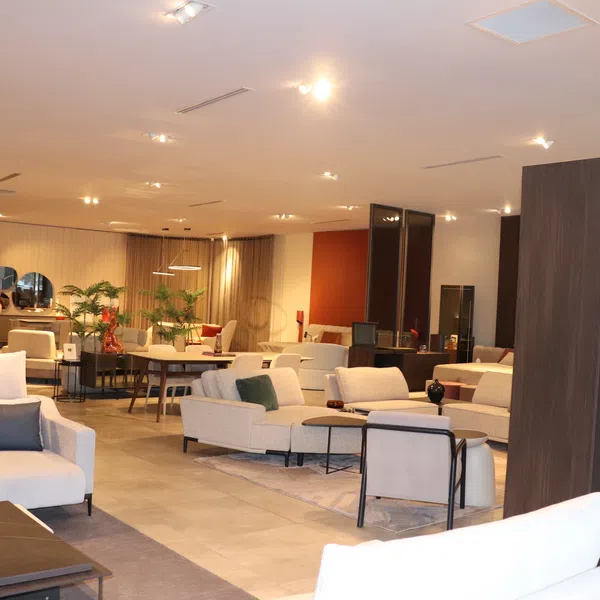 Modern living room showroom with white sofas, coffee tables, cushions, plants, and warm lighting fixtures