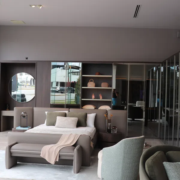 Modern bedroom with neutral tones, gray bed, green armchairs, built-in shelves, and large windows in a showroom.