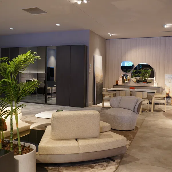 Modern living room with beige curved sofas, indoor plants, round mirrors, and a sleek dining area in soft lighting.