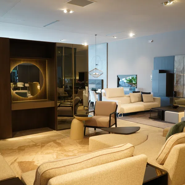 Spacious modern living room with beige sofas, armchairs, circular mirror, and warm ambient lighting.