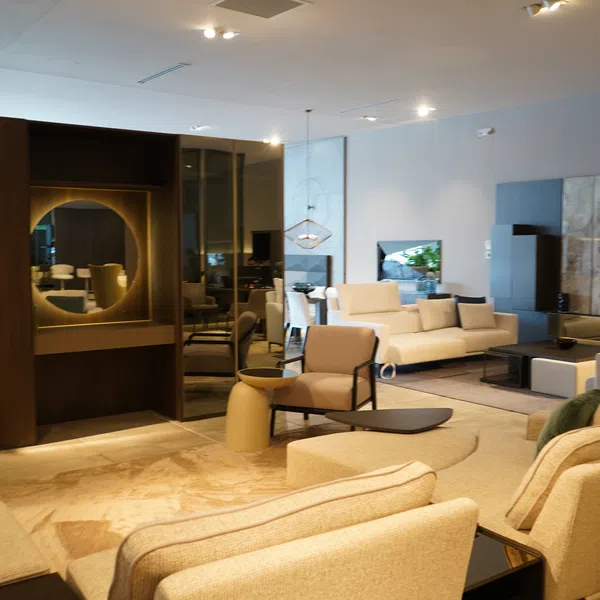 Modern living room with beige sofas, armchairs, wooden accents, glass table, and decorative round mirror on wall