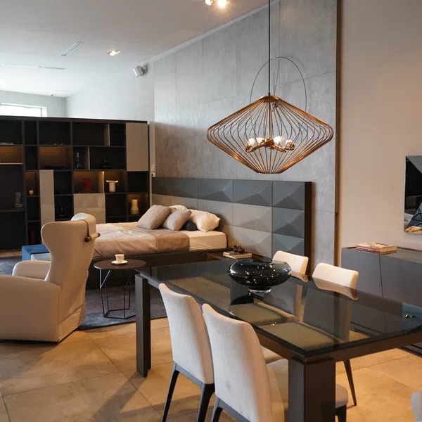 Modern open living space with dining table, chairs, armchair, bed, and stylish pendant light in neutral tones