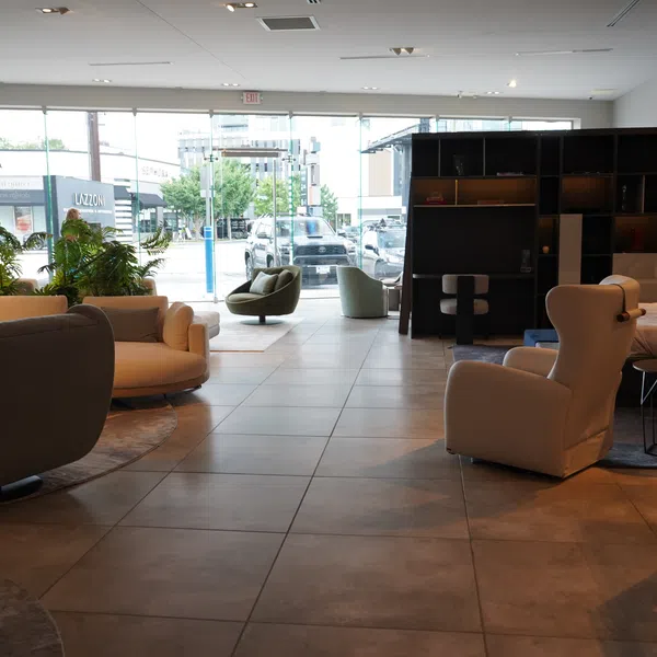 Modern furniture showroom with sofas, armchairs, a bed, and large windows overlooking a street with stores.