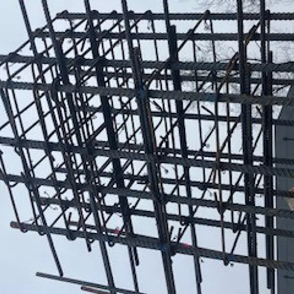 Steel rebar framework arranged for concrete reinforcement in construction site under a clear sky.