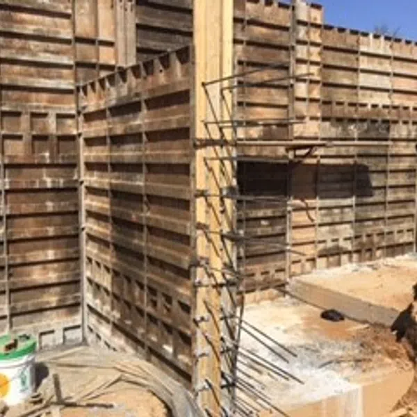 Wooden concrete formwork panels installed with rebar rods at a construction site under clear sky.