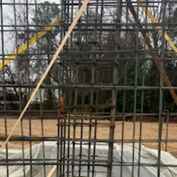 Steel rebar framework for concrete foundation with wooden supports at construction site surrounded by trees.