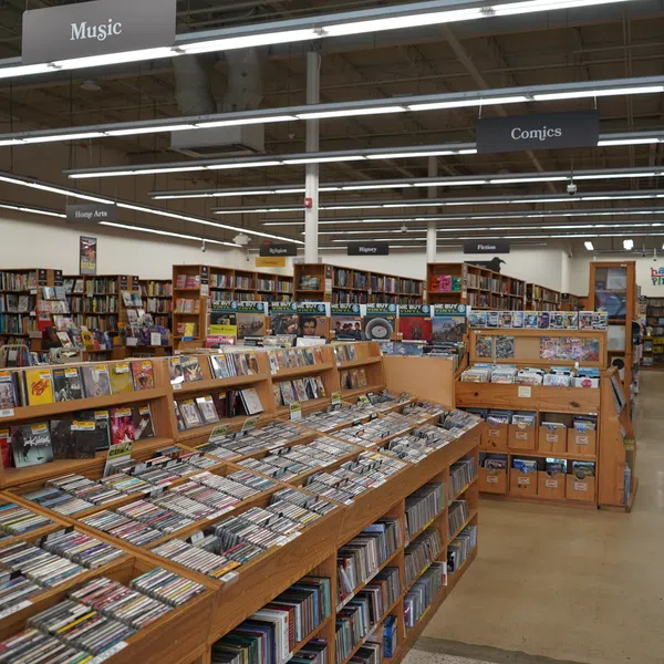 Spacious bookstore aisle with sections for music, comics, and books filled on wooden shelves under bright lighting.