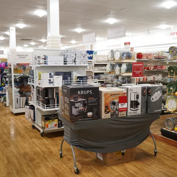 Store aisle with kitchen appliances, coffee makers on clearance, and shelves of decorative dinnerware.