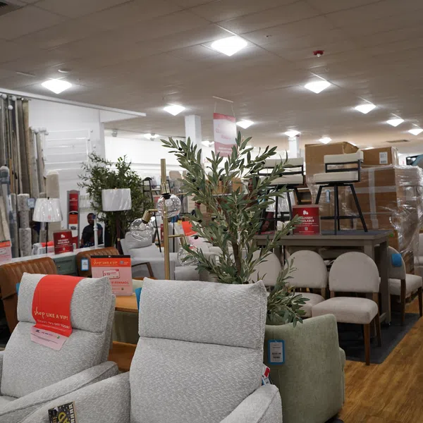 Furniture store interior with sofas, chairs, lamps, and home decor items displayed on wooden flooring under bright ceiling lights.