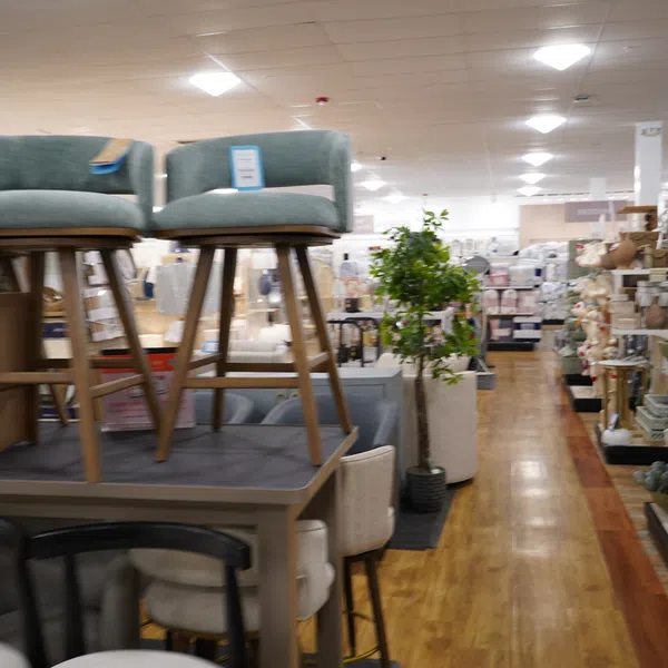 Furniture store interior with stools, chairs, tables, home decor, and wooden flooring under bright ceiling lights.