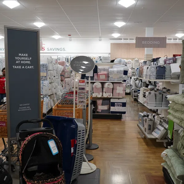 Interior of a bedding store section with shelves of blankets, pillows, and shopping carts at the entrance.