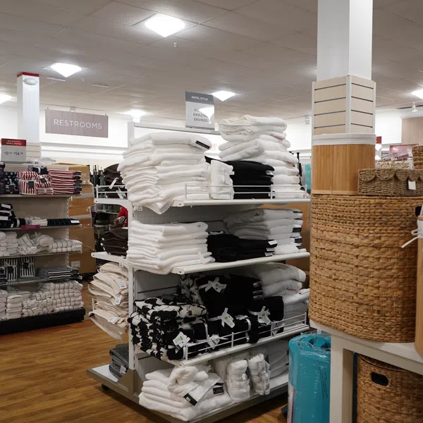 Store display with neatly folded white, black, and patterned towels and woven storage baskets on wooden floor.