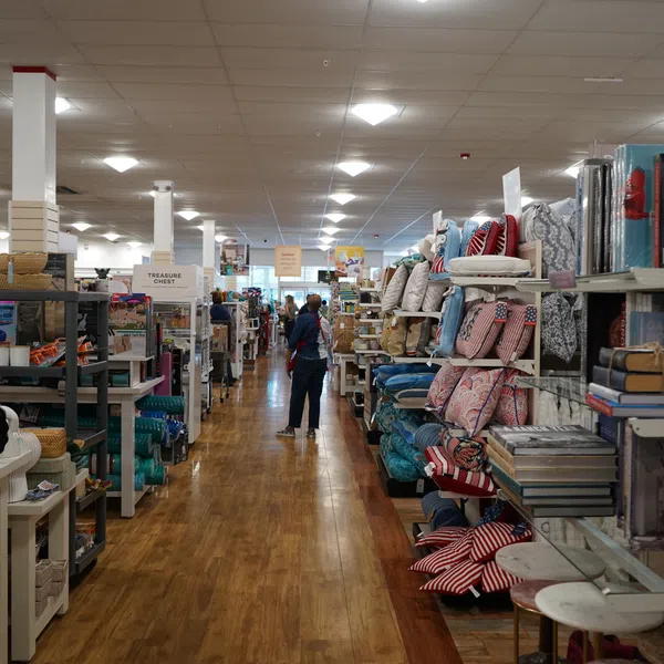 Interior of a home goods store aisle with pillows, books, and decorative items on wooden floors and shelves