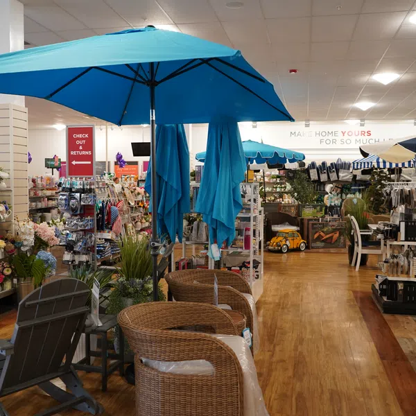 Indoor view of a home goods store featuring wicker chairs, blue umbrellas, and various decorative items on display.