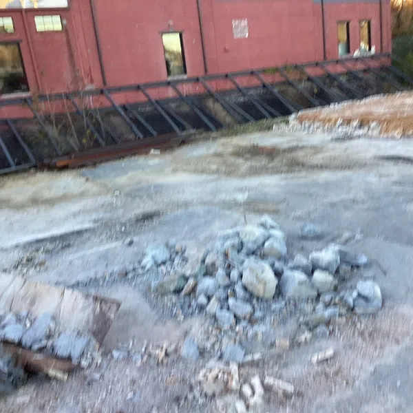Pile of broken concrete rubble on rooftop near a red brick building with windows and metal awnings.