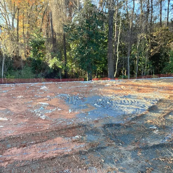 Cleared construction site with muddy ground and tire tracks bordered by a forest of tall trees in autumn light