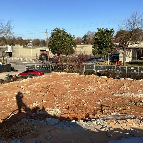 Cleared construction site with exposed dirt, debris, and shadows of a person and equipment under clear blue sky.