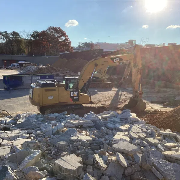 Yellow CAT excavator working on rubble at a construction demolition site under sunlight.