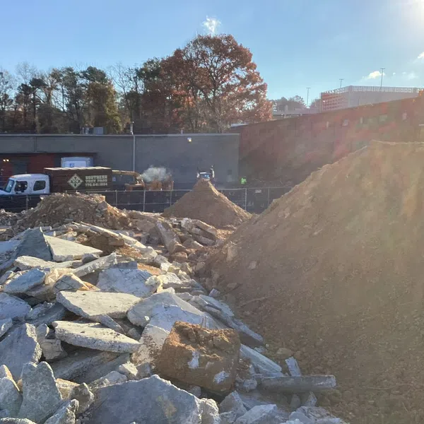 Construction site with large piles of dirt and broken concrete slabs under bright sunlight.