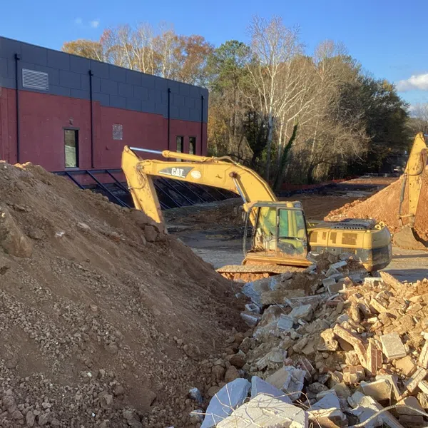 Construction site with excavators moving dirt and rubble near a modern brick and grey building under clear sky.