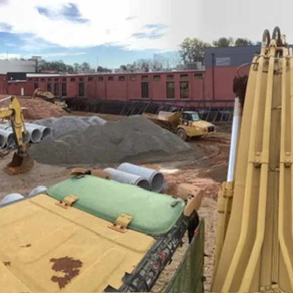 Construction site with heavy machinery, concrete pipes, and cleared land under a cloudy blue sky in an industrial area.