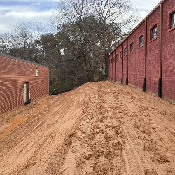 Cleared dirt pathway between two red brick buildings with bare trees in the background on a cloudy day
