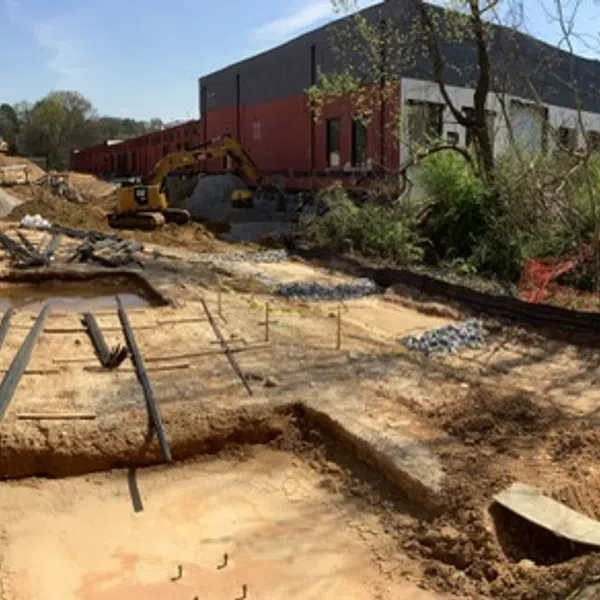Panoramic view of a construction site with steel beams, earthworks, vehicles, and nearby trees under a clear sky.