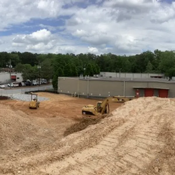 Panoramic view of a construction site with earth moving equipment and buildings under a partly cloudy sky