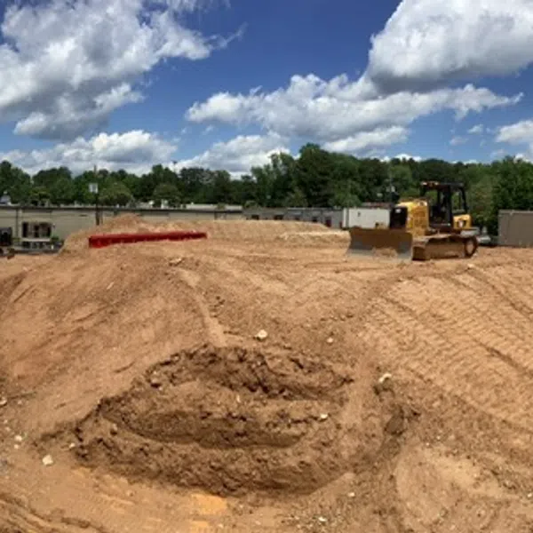 Wide panorama of an active construction site with earthworks, equipment, and partly built structures under a cloudy sky.