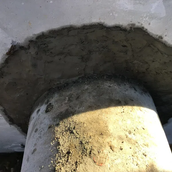 Close-up of concrete column base with fresh cement patch on surrounding floor surface in sunlight.