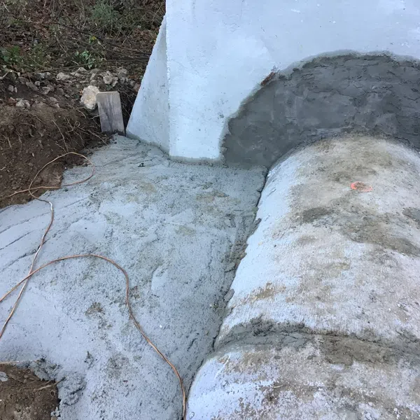Concrete drainage pipe and surrounding area under construction with fresh cement and exposed soil.