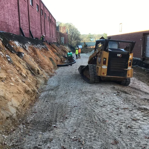 Construction site with excavation and a Caterpillar skid steer loader working between two brick buildings.