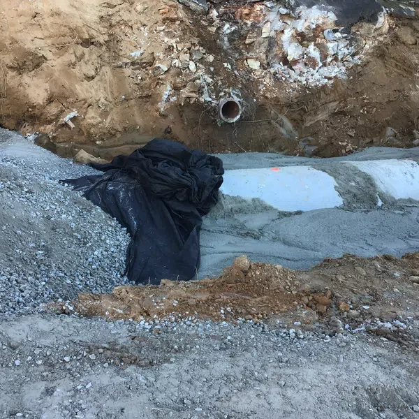 Two construction workers at a cement pipe installation site surrounded by gravel and soil during excavation.