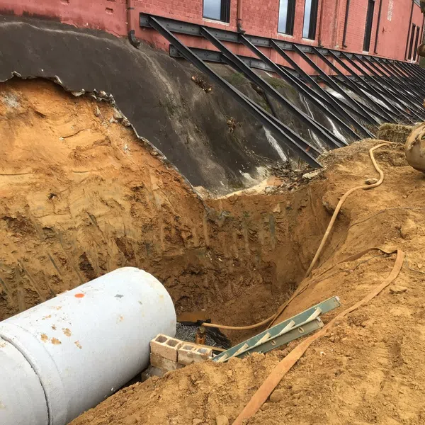 Construction site with large concrete pipe being installed beside building with metal reinforcements and excavator.