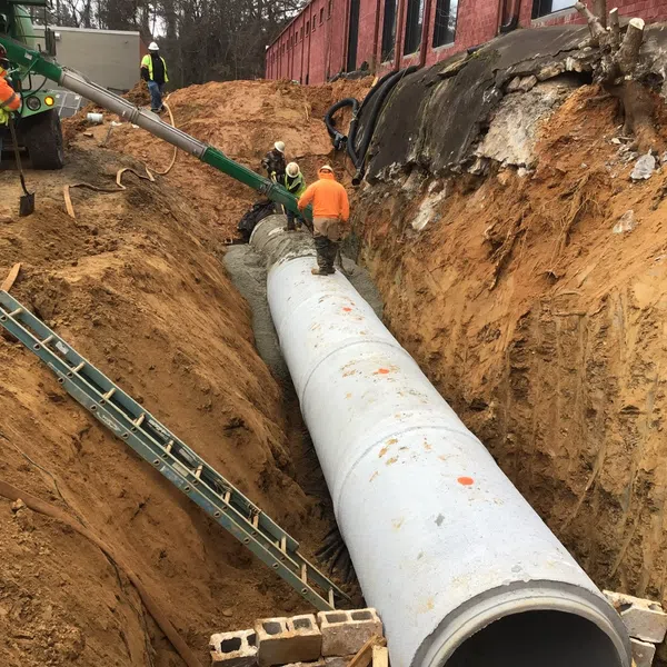 Construction workers install a large concrete pipe in a deep trench for underground infrastructure.