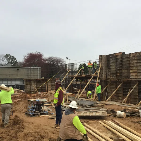 Construction workers in high-visibility clothing building wooden framework on a cloudy day at a construction site.