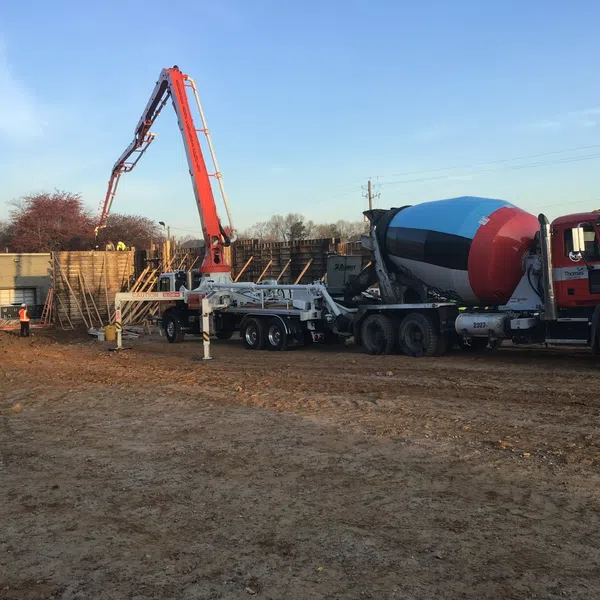 Concrete mixer truck and pump pouring concrete at construction site during daytime with workers present.