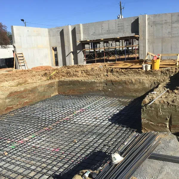 Construction site with foundation rebar grid, excavated soil, and concrete building walls under clear blue sky