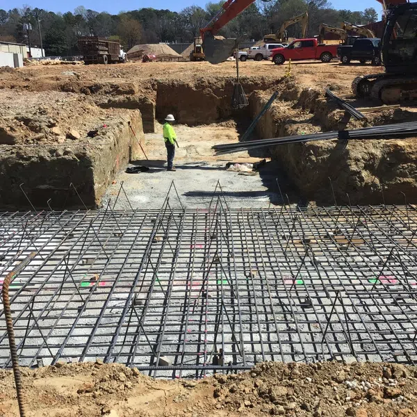 Construction site with steel rebar grid foundation, workers, and excavators preparing ground for building.