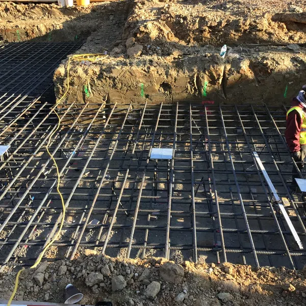 Construction workers installing steel rebar grid for concrete foundation on a sunny earth excavation site.