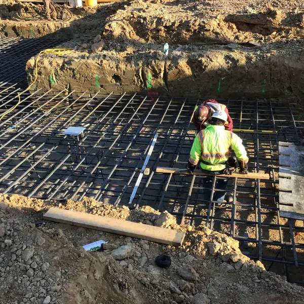 Construction workers installing steel rebar grid for concrete foundation at a building site with dirt and equipment.
