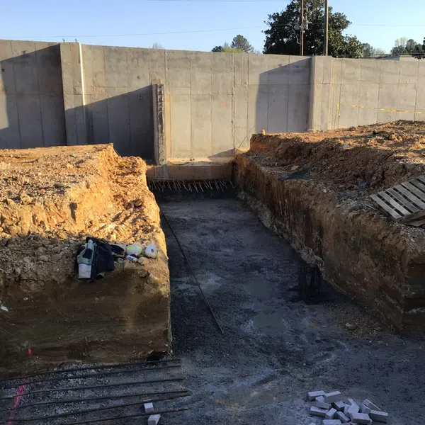 Excavation site with earth trenches and concrete foundation walls for a construction project under sunlight.