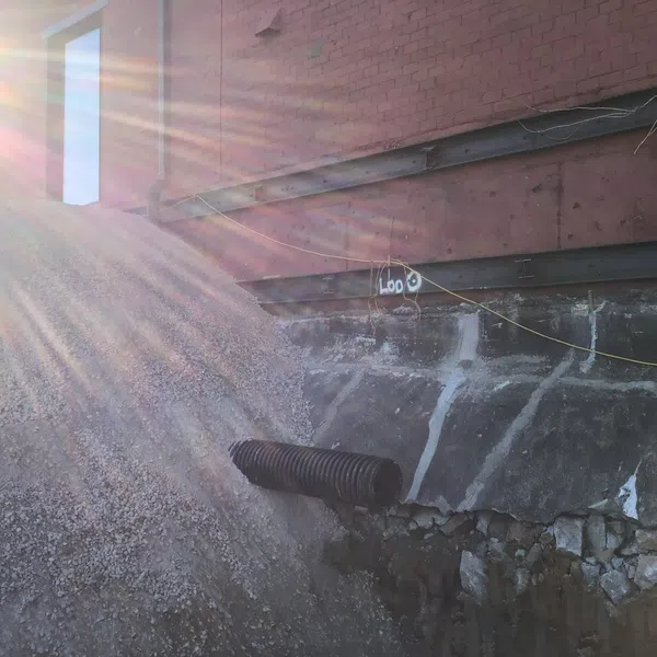 Sunlight beams over gravel pile with drainage pipe by brick building under construction