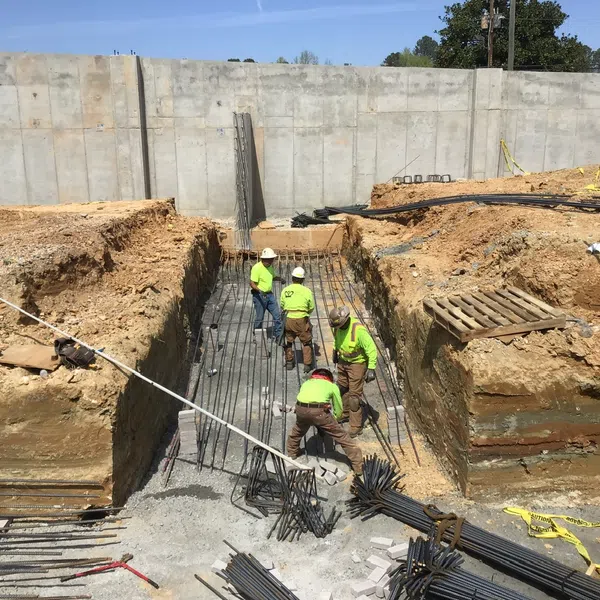 Construction workers install rebar in deep trench foundation at a commercial building site on a sunny day