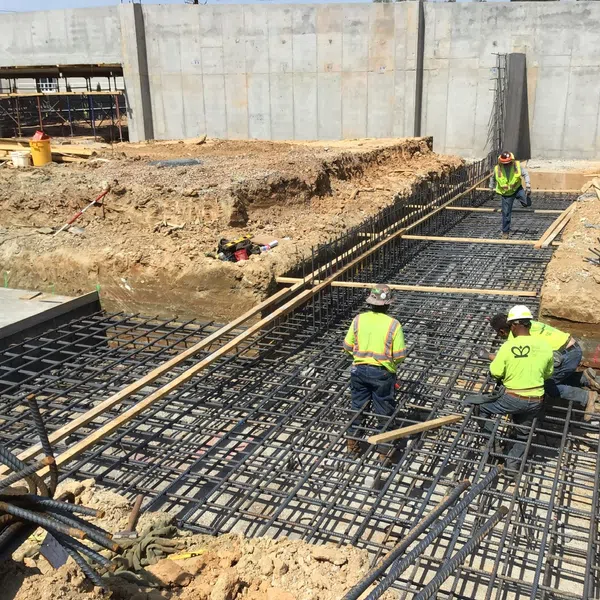 Construction workers installing steel rebar grid for concrete foundation at a large building site under clear weather.